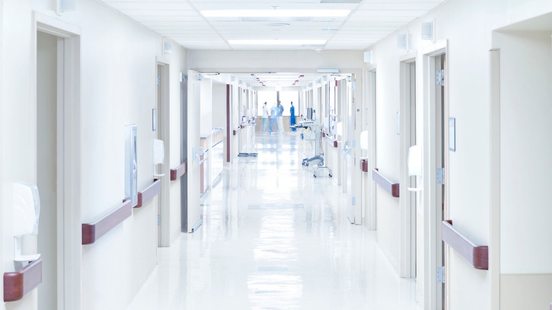 Heller Krankenhausflur mit Patientenzimmern auf beiden Seiten und medizinischem Personal im Hintergrund