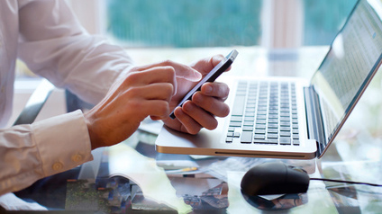 Mann mit Smartphone vor einem Laptop